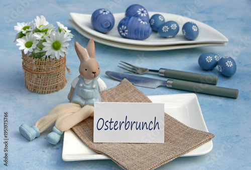 Gedeckter Tisch zum Osterbrunch mit blauen Ostereiern, Hasenfigur und Karte mit der Beschriftung Osterbrunch.