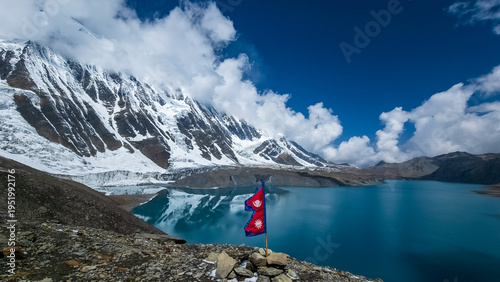 Nepal Flag fluttering in the wind at Lake tilicho, highest lake in the world, with himalayan mountains and glaciers in the background