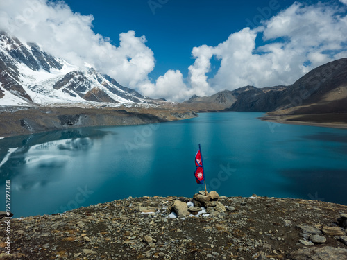 Nepal Flag fluttering in the wind at Lake tilicho, highest lake in the world, with himalayan mountains and glaciers in the background