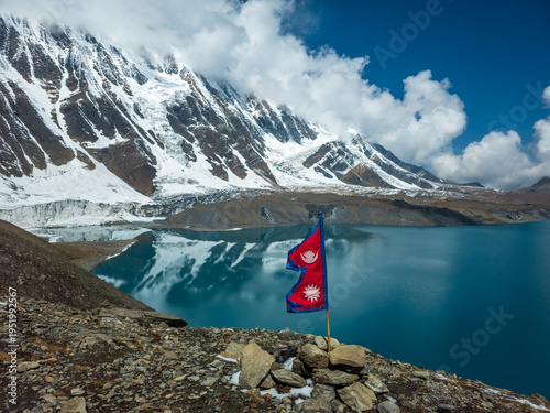 Nepal Flag fluttering in the wind at Lake tilicho, highest lake in the world, with himalayan mountains and glaciers in the background