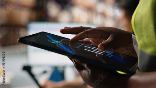 Obraz na płótnie Close up of african american person checking tracking info for parcels on tablet, ensuring correct shipment address for express delivery services in warehouse