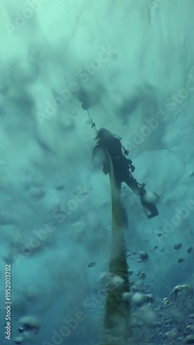 A scuba diver is captured gracefully descending along a line in the vast, blue ocean. Sunlight filters through the water, creating a beautiful, ethereal effect as they explore.