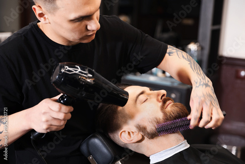 Принти на полотні Stylist blow drying man's beard in barbershop