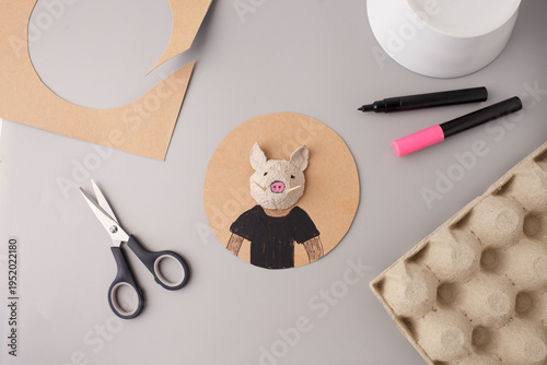 DIY wild boar character craft made from recycled egg carton on cardboard. Sustainable handmade toy for kids art school project and environmental education. Creative upcycling hobby activity