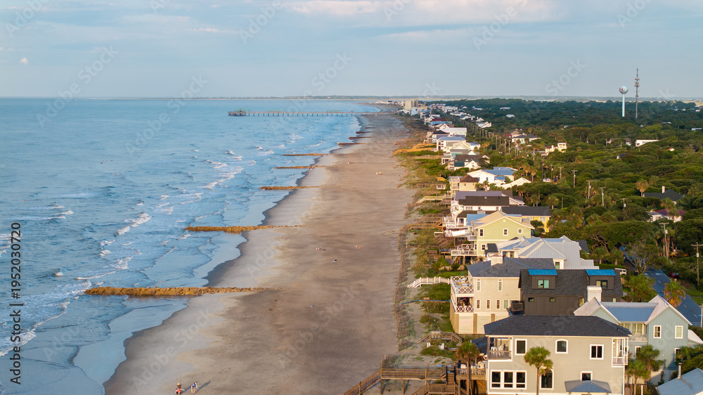Fototapeta premium Aerial view of shoreline and landscape of Folly Beach town near Charleston, South Carolina showcasing the coast, pier, and beach homes during morning sunrise