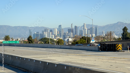 Downtown LA skyline viewed from the 110 freeway with mountains behind under clear blue sky