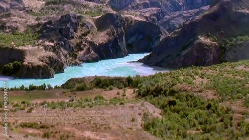 A stunning panorama unveils a crystalline, turquoise river snaking through the arid Patagonian landscape of Los Alerces National Park on a clear, sunny afternoon.