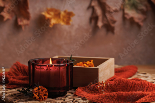Burning red candle and wooden tray with marigold petals and autumn leaves in cozy seasonal setting