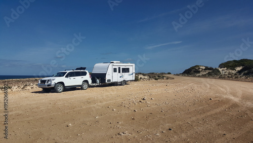 4x4 towing a caravan parked on a remote coastal road under blue sky