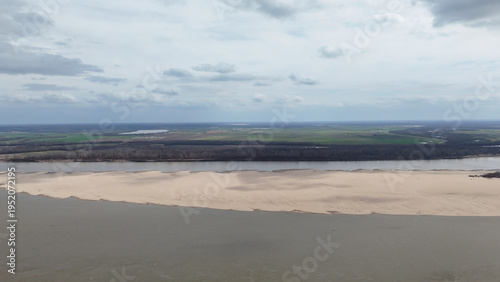 Aerial view showcasing the expansive mississippi river with prominent sandbars, dense forest on the opposite bank, and distant agricultural fields under a cloudy sky in vidalia, louisiana
