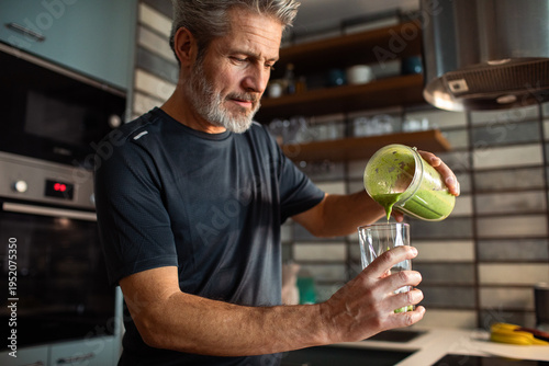 Mature man pouring green smoothie in home kitchen
