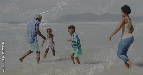 Family splashing in shallow surf, boy kicking, father splashing, mother joining for play in travel
