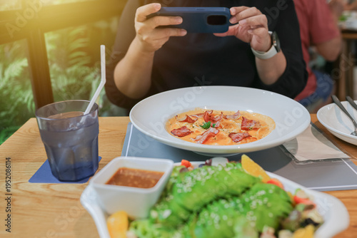 Female use smartphone take a photo and share to social media before eat spaghetti carbonara, Creamy pasta carbonara with bacon bits and fresh parsley garnish served in white bowl. Classic Italian cuis