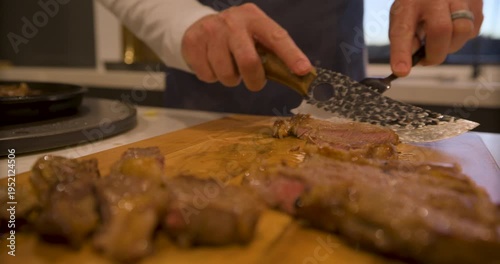 Low, closeup shot of cook quickly cutting up steaming steak on wood board