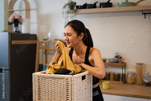 Foto Woman smelling musty laundry from basket at home, reacting to bad odor from damp