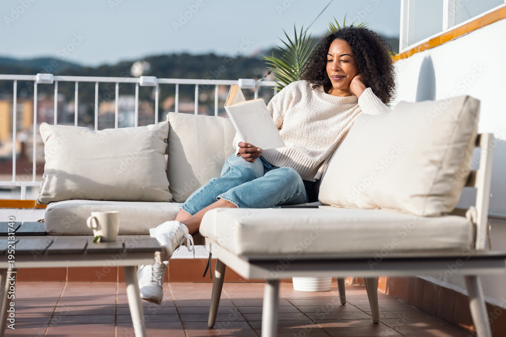 Obraz premium Relaxing woman reading a book while resting on the couch on her balcony at home