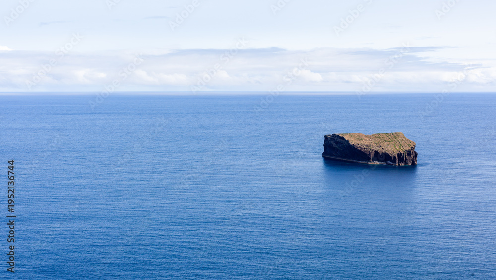 Fototapeta premium Small rocky islet in the Atlantic Ocean. San Miguel Island, Azores, Portugal. Volcanic landscape surrounded by blue sea.