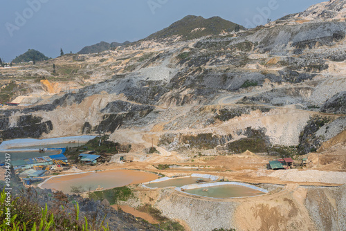 Closer view of terraced mining slopes with sediment ponds, exposed mineral layers, and small industrial structures within a large tungsten extraction site.