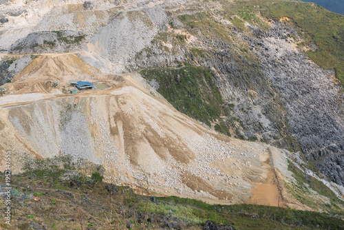 Fotografi Detailed section of a mined hillside showing loose rock, soil erosion, and a small structure on terraced slopes within a tungsten quarry environment