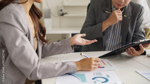 Close up of colleagues reviewing business documents and graphs while using a digital tablet. Concept of teamwork, analytics, and decision making.