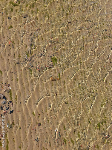 Ripples and textures seen in sand and water during low tide at a coastal area on a sunny day with clear sky