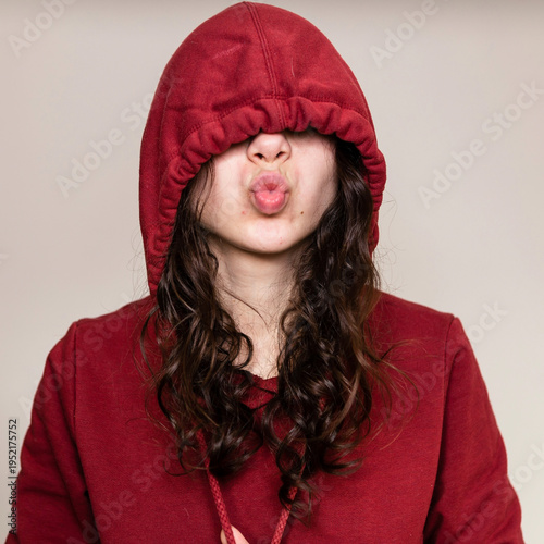 Bild auf Leinwand Girl with curly hair wearing a red hoodie makes a funny face with lips puckered
