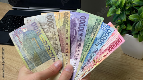 Quadro su tela A man holds Indonesian rupiah banknotes of various denominations on his desk