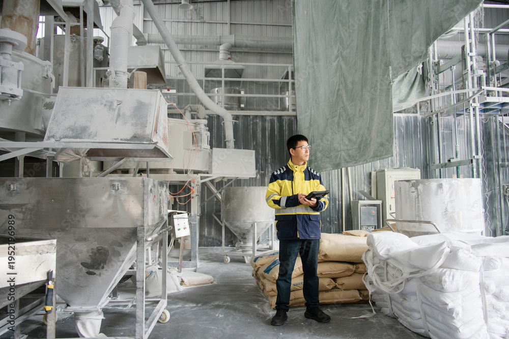 Fotografie Factory worker holding tablet while inspecting machinery in industrial workshop