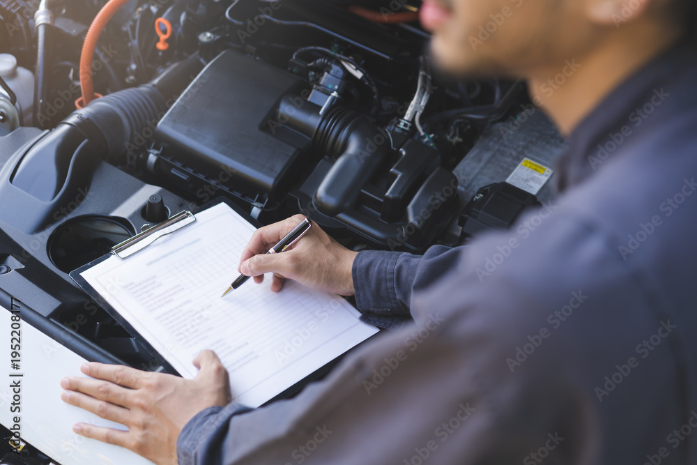 Obraz premium Auto check, car service shop concept. Automobile repairman writing job checklist on clipboard, mechanic checking engine to estimate repair machine, inspecting maintenance by engineer at vehicle garage