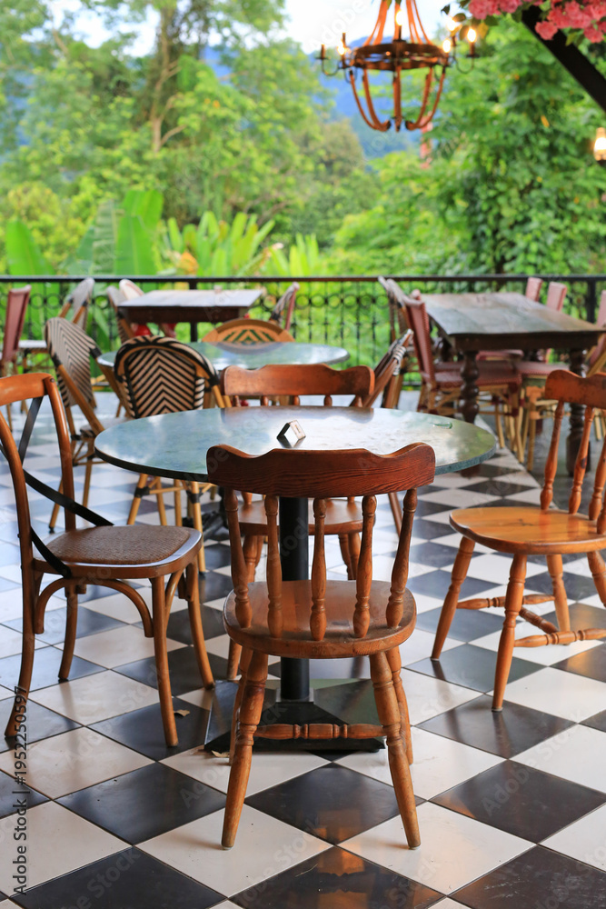 Obraz premium Empty bistro tables and woven chairs sit quietly on a balcony, waiting for guests to enjoy a meal overlooking the lush tropical forest and distant mountains.