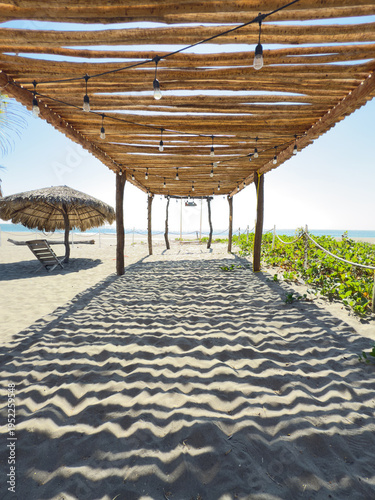 Beach pergola with wooden roof casting shadows on sand