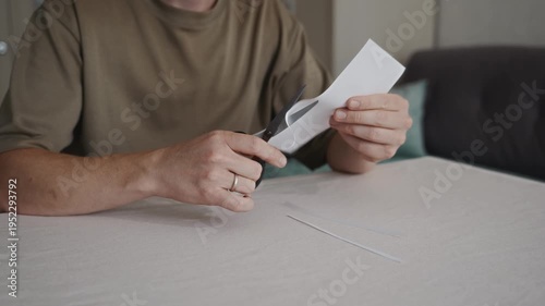 Wallpaper Mural Person sitting at a table using scissors to cut a sheet of white paper. Calm indoor scene demonstrating simple manual cutting process used in craft or office work. High quality 4k footage Torontodigital.ca