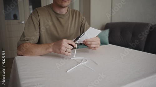 Wallpaper Mural Man sitting at a table cutting white paper with scissors while small paper pieces lie on the table. Everyday indoor activity showing simple manual work. High quality 4k footage Torontodigital.ca