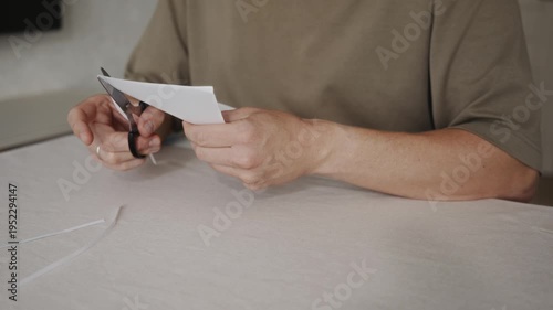 Wallpaper Mural Man begins cutting a sheet of white paper with scissors while sitting at a table. The blades close on the edge of the paper as the cutting process starts. High quality 4k footage Torontodigital.ca
