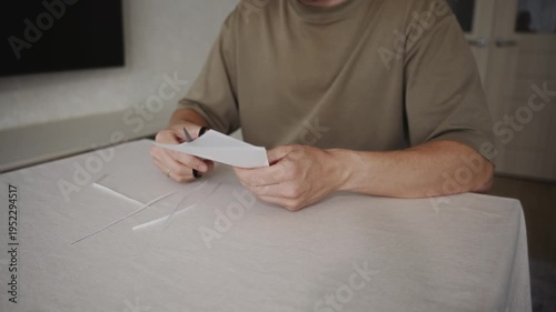 Wallpaper Mural Man continues cutting a piece of white paper with scissors while sitting at a table. Paper strips accumulate on the table as the blades repeatedly close and open during the cutting process. 4k footage Torontodigital.ca