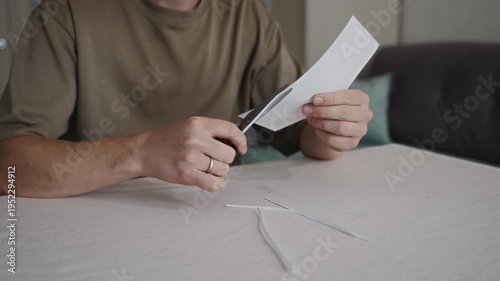 Wallpaper Mural Man sitting at a table cutting white paper with scissors while small paper pieces fall onto the table. Everyday indoor activity showing simple manual work. High quality 4k footage Torontodigital.ca