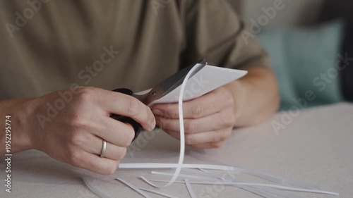 Wallpaper Mural Close-up of hands cutting a curved strip from a sheet of white paper using scissors. Small paper pieces lie on the table during simple craft or office activity. High quality 4k footage Torontodigital.ca