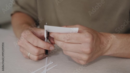 Wallpaper Mural Close-up of hands cutting small strips from a white sheet of paper using scissors. Thin pieces of paper fall onto the table during a simple craft or office activity. High quality 4k footage Torontodigital.ca