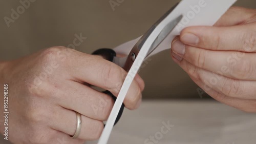 Wallpaper Mural Close-up view of scissors cutting a narrow strip from a sheet of paper. Hands carefully guide the blades demonstrating a simple manual cutting process used in crafts or office work. High quality 4k Torontodigital.ca