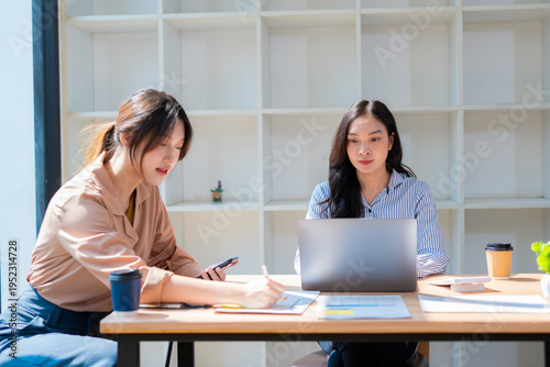 Group of happy Asian business people having a meeting at the office. Two women working together using modern laptops.