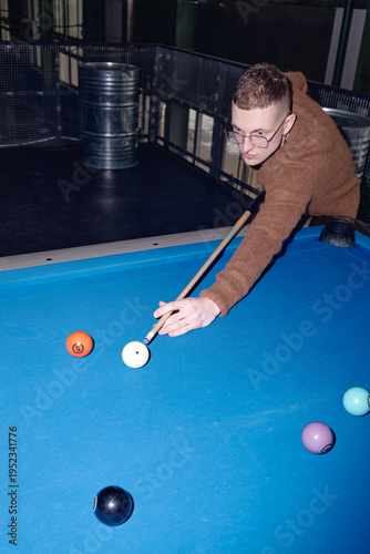Foto Vertical shot of young adult Caucasian man playing billiards, leaning over blue