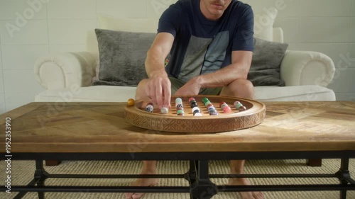 Man relaxes in a luxury home while playing an ornate wooden Solitaire table game on a nice wooden coffee table.