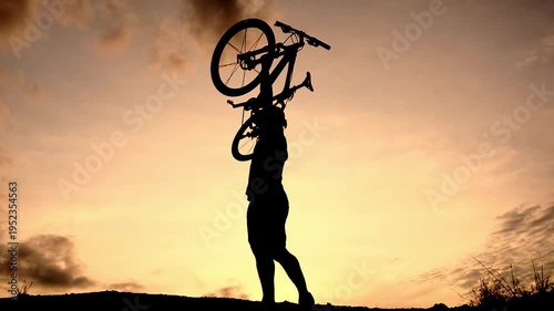 Silhouette of person carrying bicycle against the sunset sky. The person is holding the bike over their head