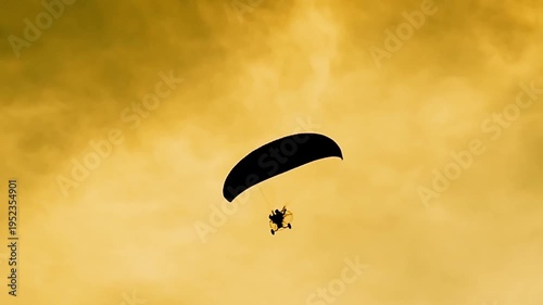 A silhouette of a paraglider soaring through the golden sky. The person appears small against the vast expanse, gliding effortlessly