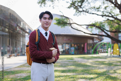 Young asian man student standing on campus holding book