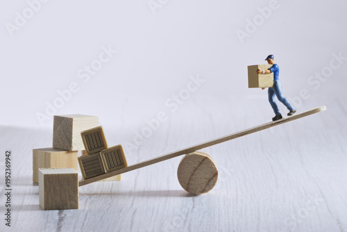 Foto Miniature worker carrying a box on an unbalanced seesaw structure