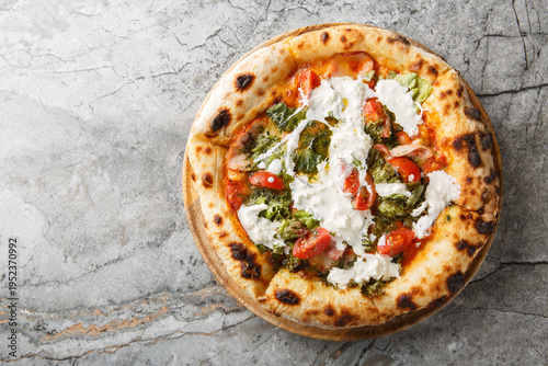 Foto Delicious authentic pizza with stracciatella cheese, pesto, ham and cherry tomatoes close-up on a wooden board on the table