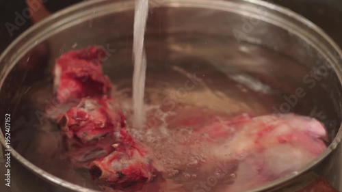 Fresh beef bones in a pot are gradually filled with cold running water. Preparing meat ingredients for long simmering of a rich homemade broth