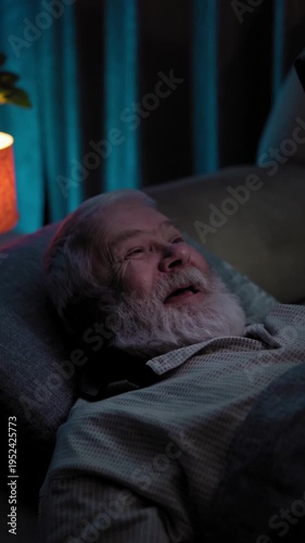 In dark room in bed, an old man react emotionally to video content on his phone