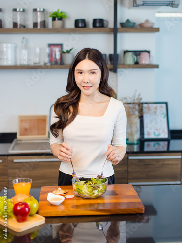 Asian young pretty positive woman standing in kitchen prepare making eating healthy salad from glass bowl cooking healthy food fresh vegetables fruits clean feel good morning happy relaxing lifestyle.